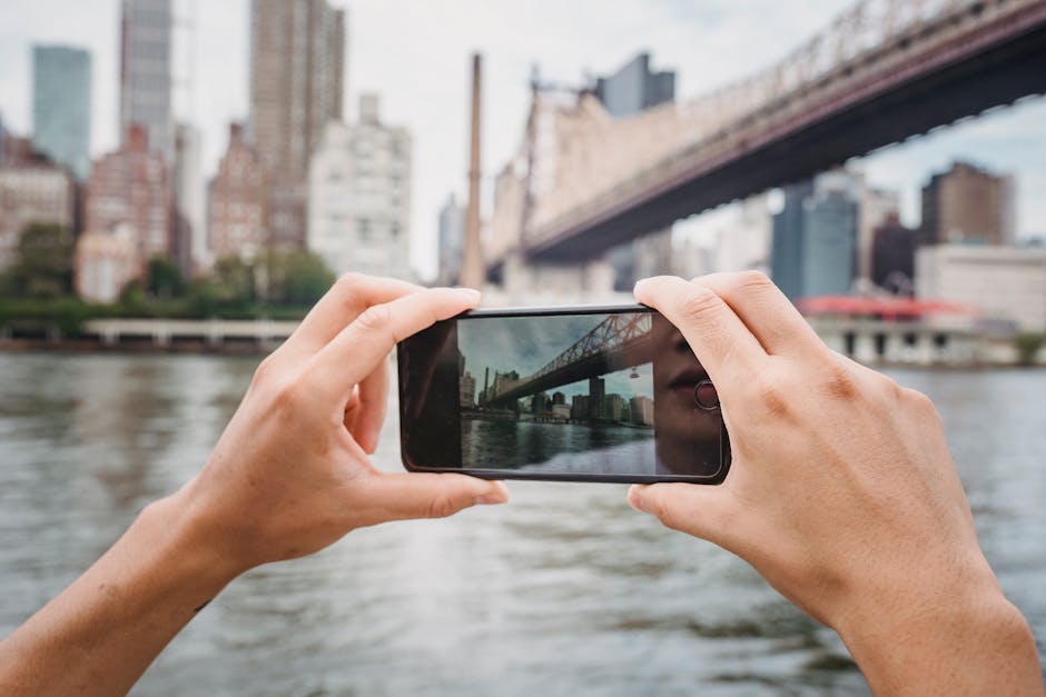 Crop unrecognizable traveler taking photo of modern suspension bridge in city using mobile phone in daytime