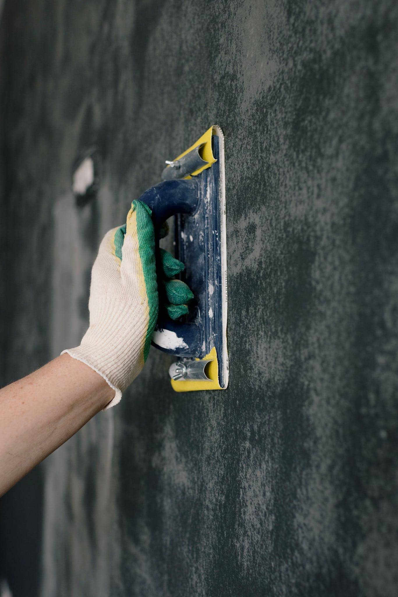 Crop anonymous male worker in gloves holding scraper and aligning walls in flat