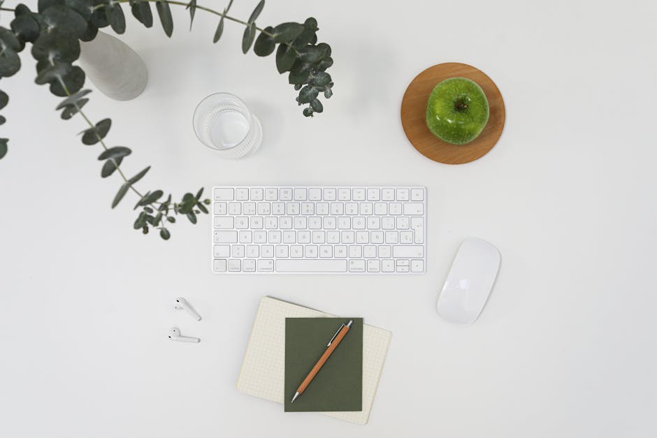 From above of modern wireless devises placed on white table among notebooks and vase with branch of eucalyptus and ripe green apple