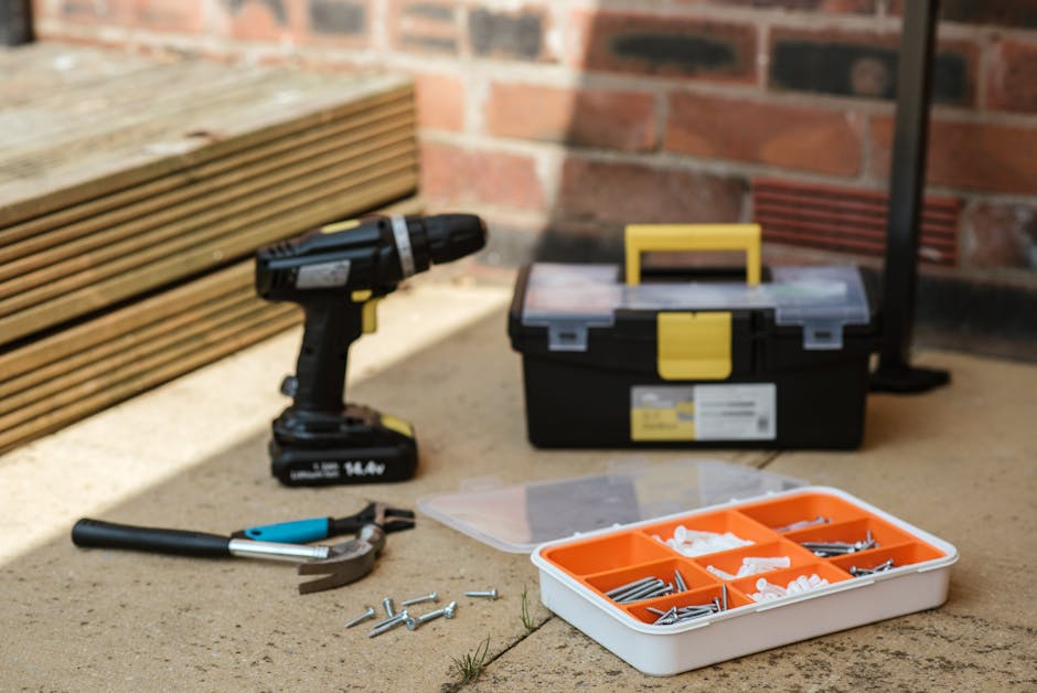 Electric screwdriver on floor near containers with instruments placed near spanner with hammer against brick wall  and wooden barrier