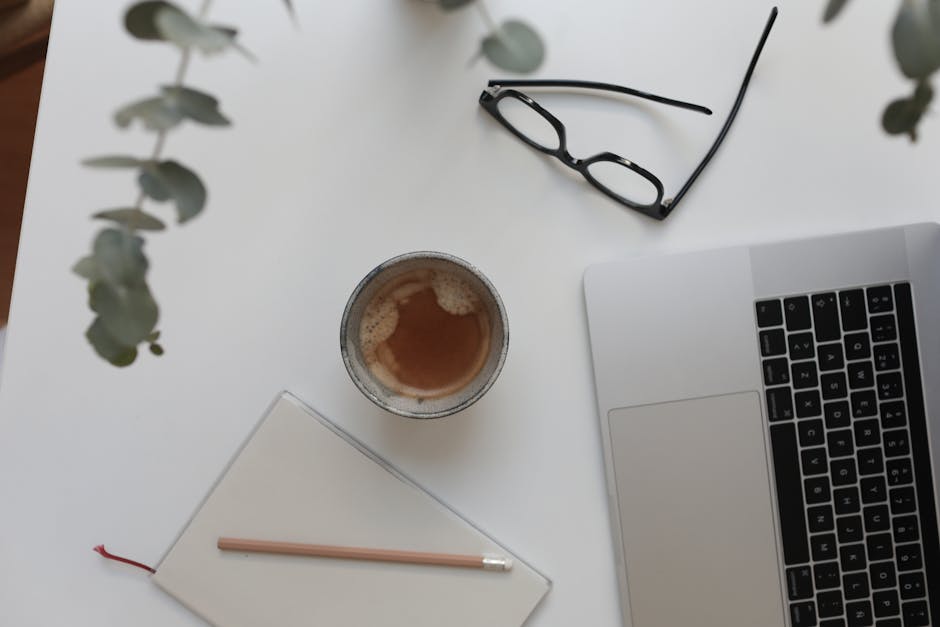 From above of cup with hot drink near netbook and notepad under plant