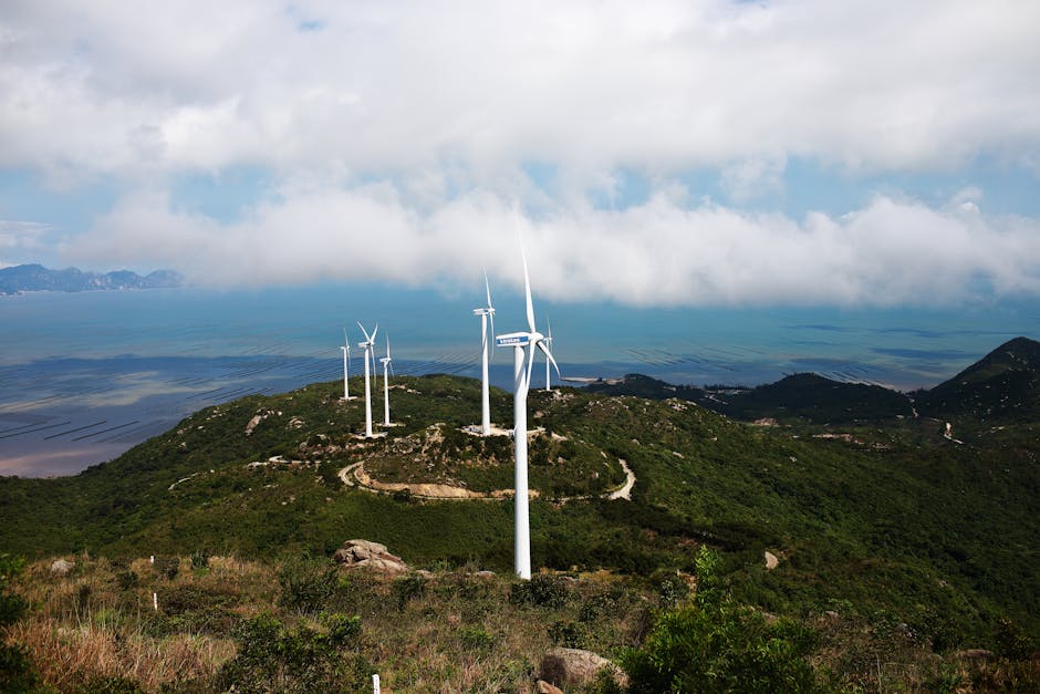 Picturesque scenery of wind turbines located on grassy hill in mountainous terrain against cloudy blue sky