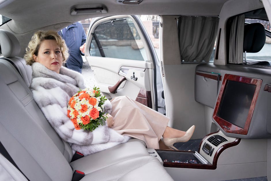 Cheerful female with curly hair wearing dress and fur coat sitting in passenger seat of luxurious car with opened door with bouquet of colorful flowers