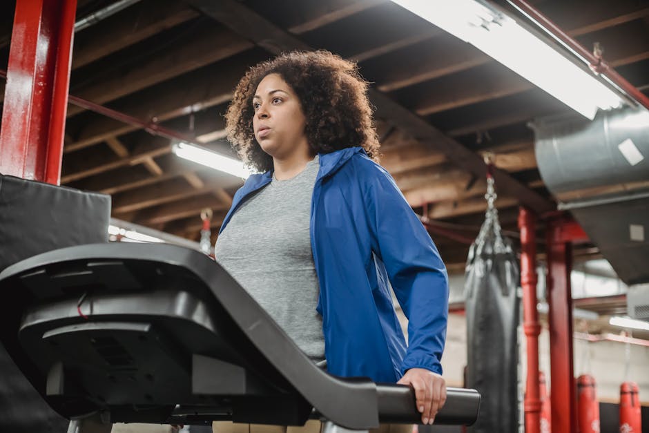 Low angle of plump African American female standing on treadmill in gym and looking away