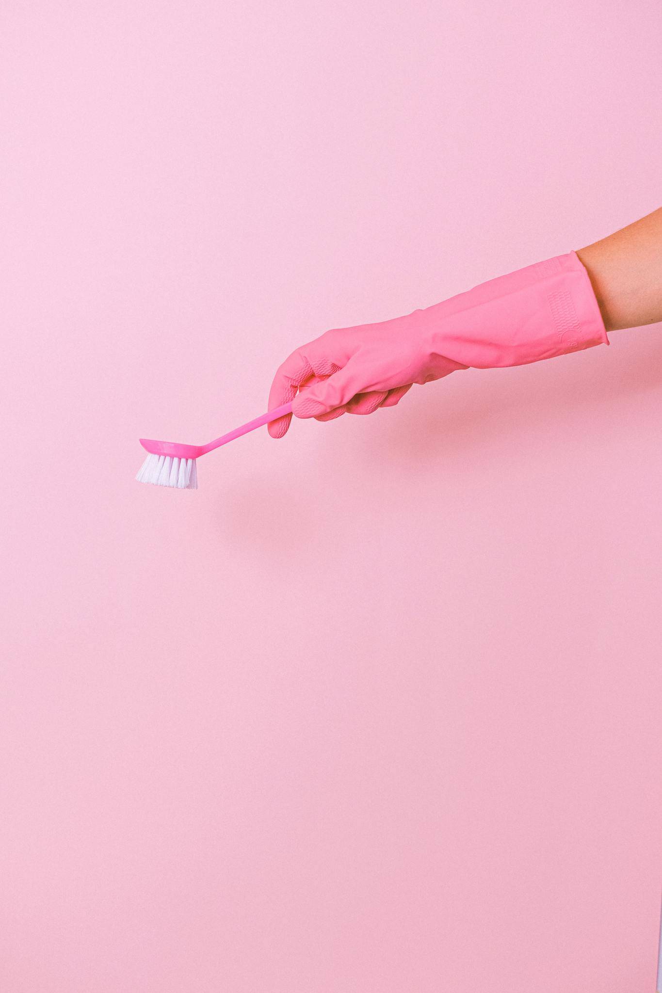 Unrecognizable cleaner wearing protective glove using plastic brush in hand to remove dirt during household against pink background in studio