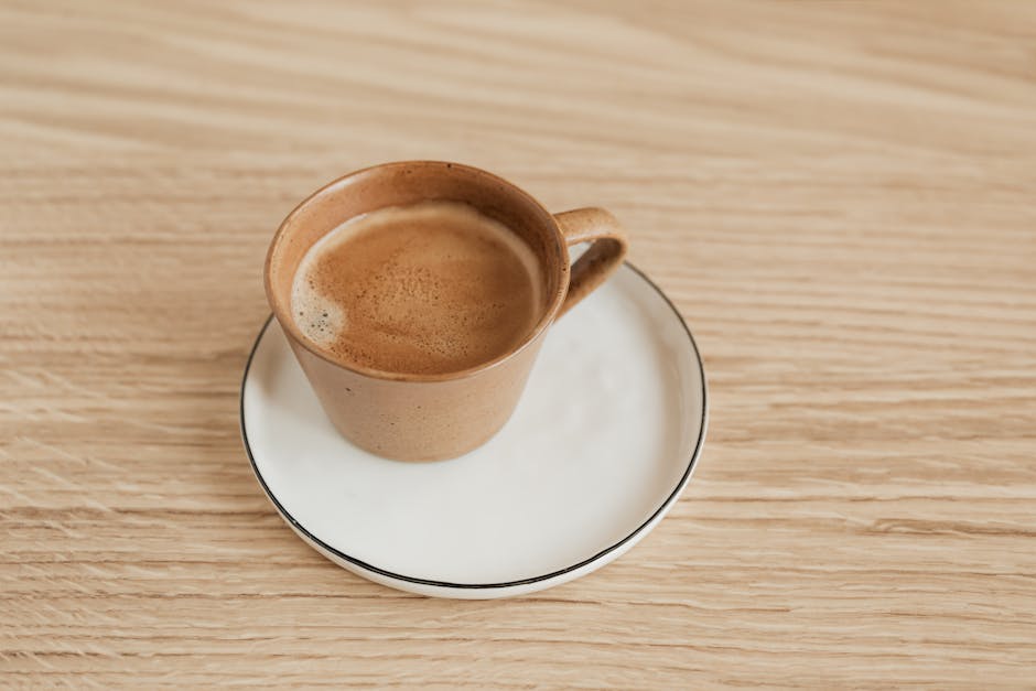 From above of beige ceramic cup of aromatic espresso on white elegant saucer with thin black edge placed on wooden surface