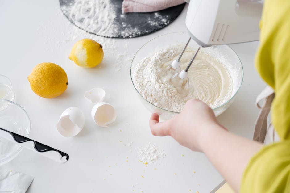 From above of crop anonymous female with mixer preparing cake dough at table with fresh lemons and eggshells in house