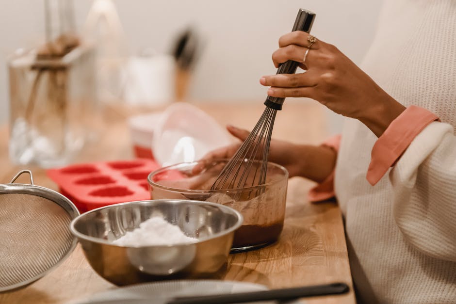 Side view of crop anonymous African American female whisking melted chocolate near metal bowl with flour in kitchen