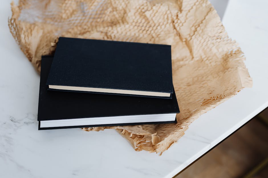 From above of notebook pair with black empty hardcover placed with packing paper and white marble table during prepare for postal delivery