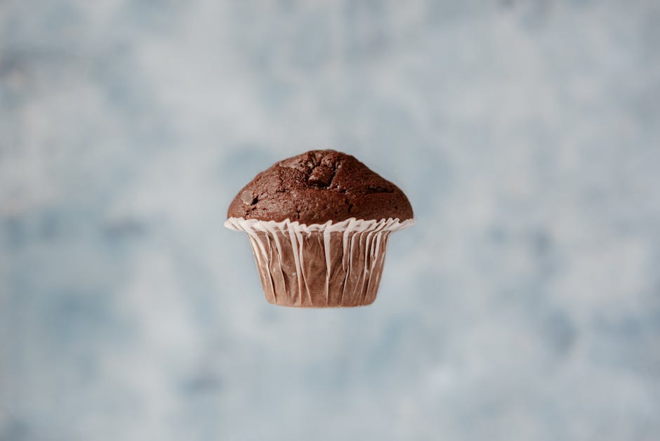 Sweet chocolate muffin hanging in air on blurred background