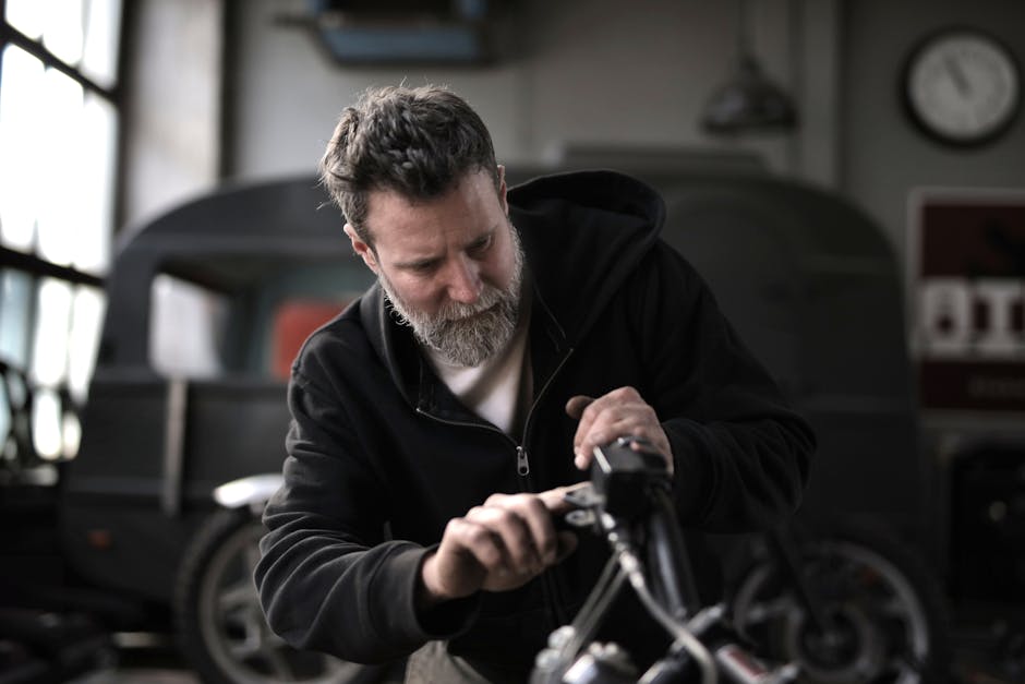 Concentrated male biker in casual wear fixing motorcycle part while working in garage