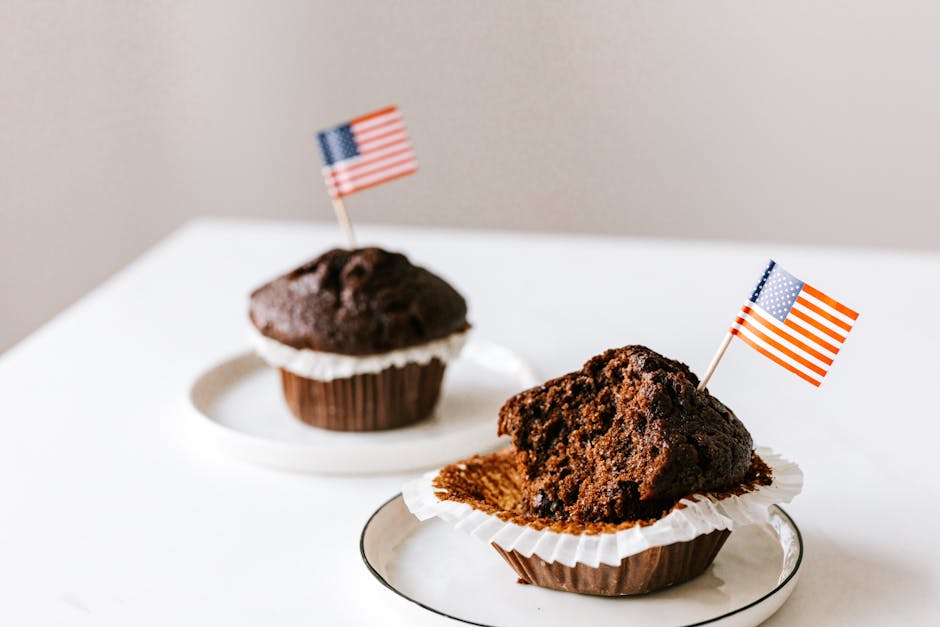 From above of bitten and whole festive chocolate cupcakes decorated with miniature american flags and placed on white table