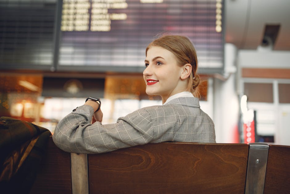 Side view of positive female manager waiting for flight on wooden seat in airport
