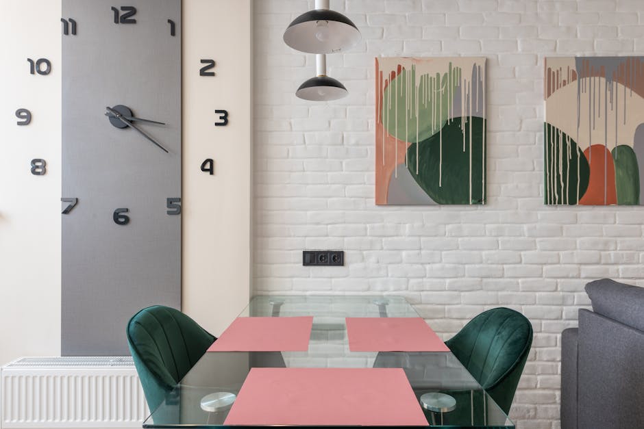 Interior of contemporary creative dining room with glass table and soft chairs placed near brick wall with clock and paintings