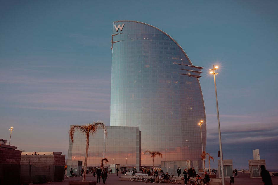 Contemporary building facade in form of sail against streetlights and anonymous people walking under sunset sky in Barcelona Spain