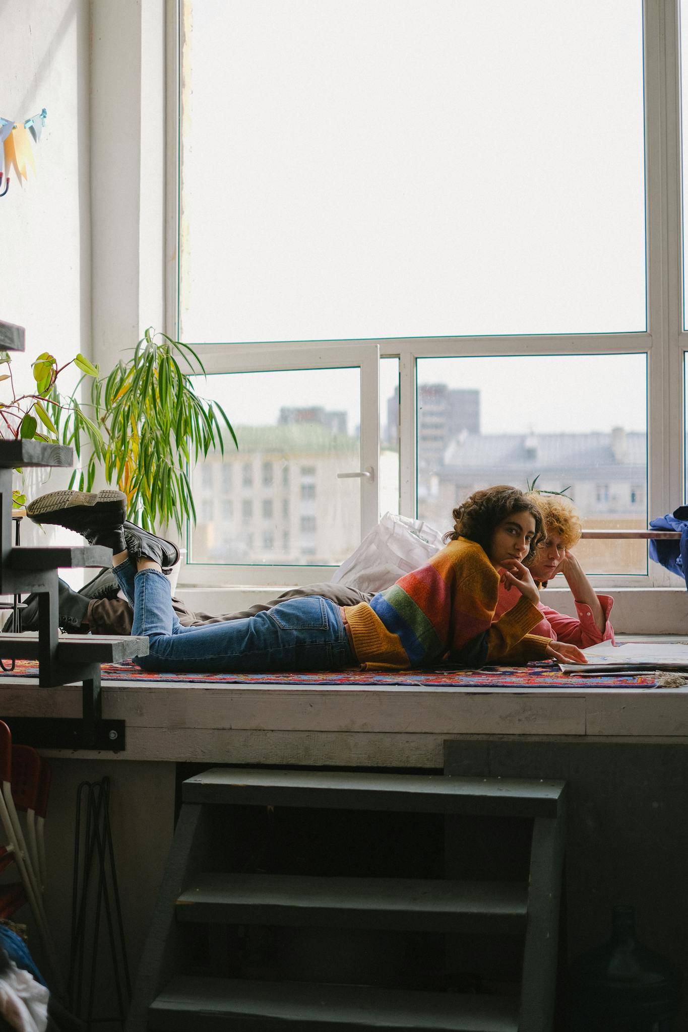 Side view of young designers lying on big windowsill and watching sketchbook in arts craft shop