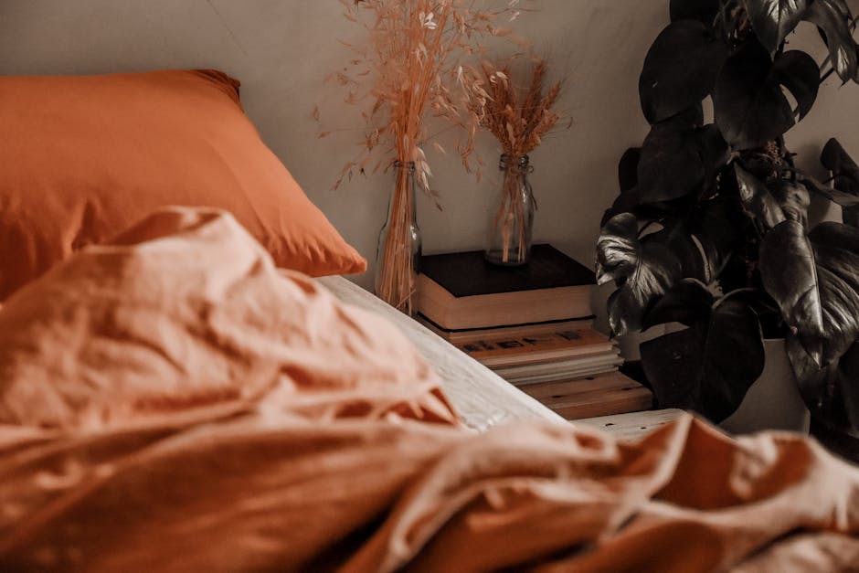 Interior design of bedroom with pillow and blanket on bed and books with dried herbs in bottles on side table and big plant near window