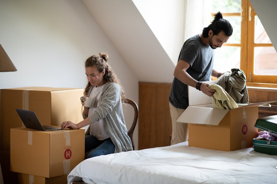 Pensive female surfing internet on netbook and drinking coffee while ethnic man unpacking belongings from cardboard box after moving into new attic style house