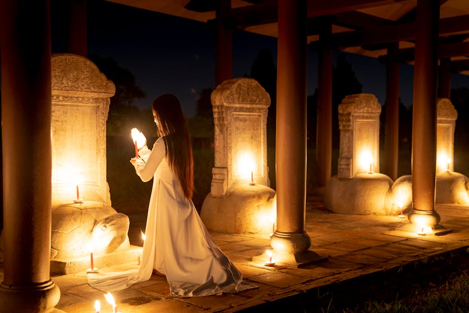 Full body back view of anonymous female with burning candles standing on knees near stone turtles while praying in dark time