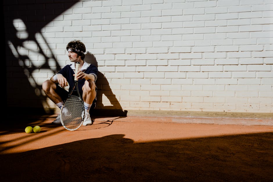 A Man Holding a Tennis Racket Sitting by a Brick Wall