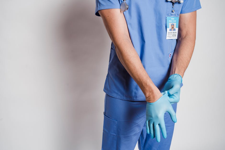 Crop anonymous male doctor in uniform with stethoscope putting on sterile gloves while standing near white wall in hospital