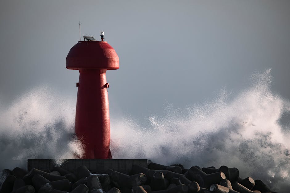 Red Lighthouse over a Stack of Concrete Buoys and Wave Splash