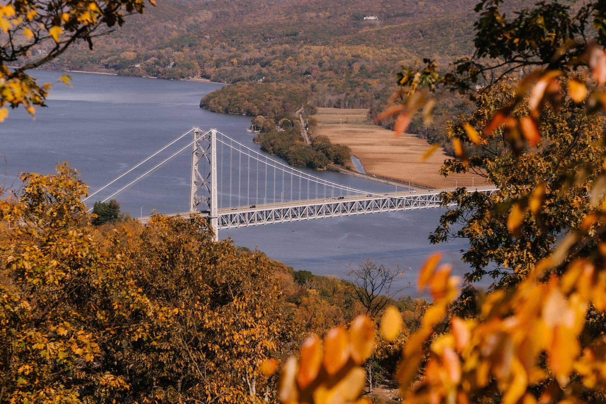 Suspension bridge over calm river flowing through hilly terrain covered with lush autumn trees