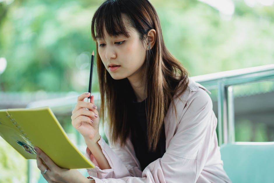 Crop focused ethnic female student with workbook and pencil studying on chair in sunlight