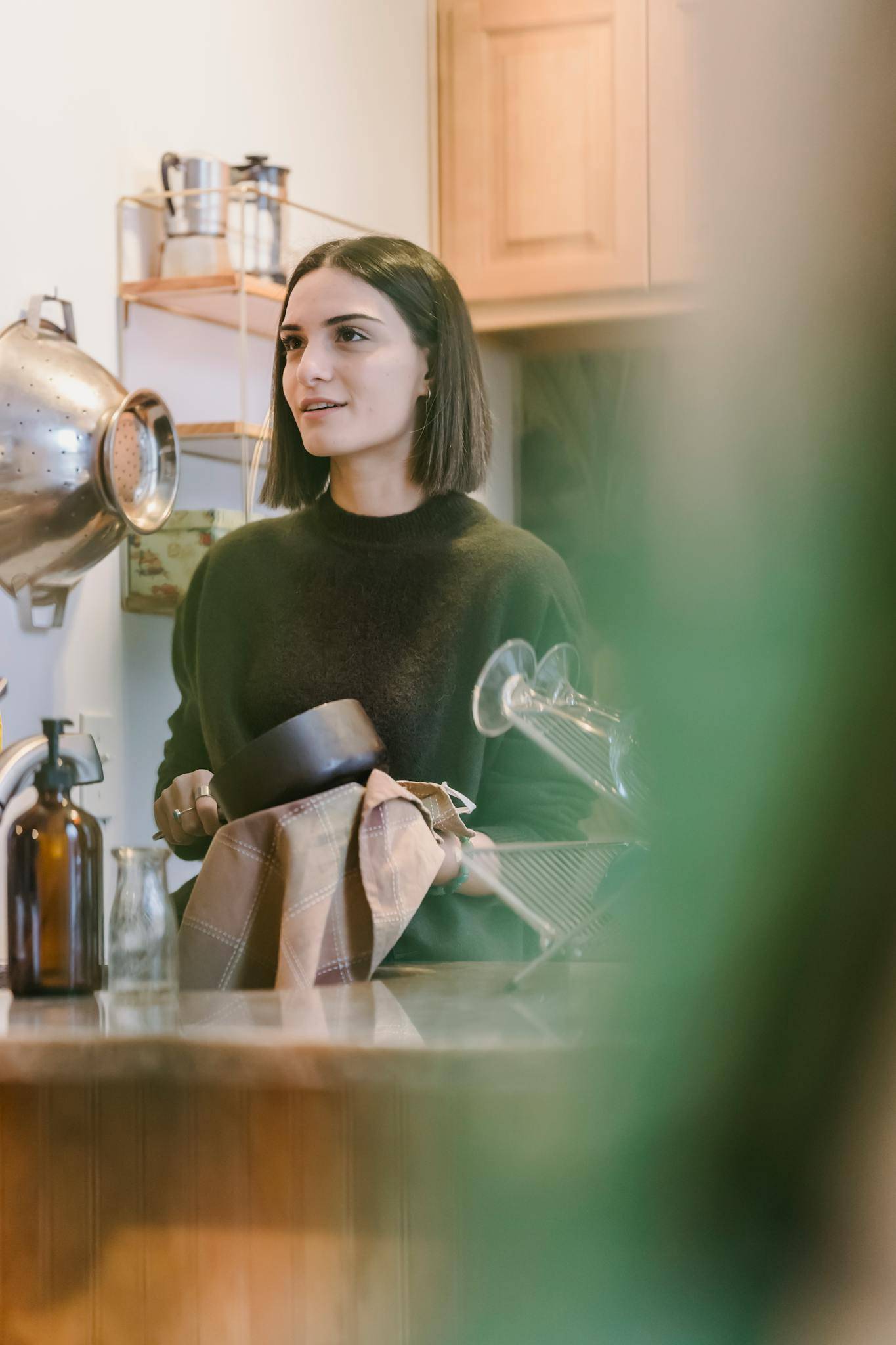 Content young housewife drying utensil with towel in kitchen