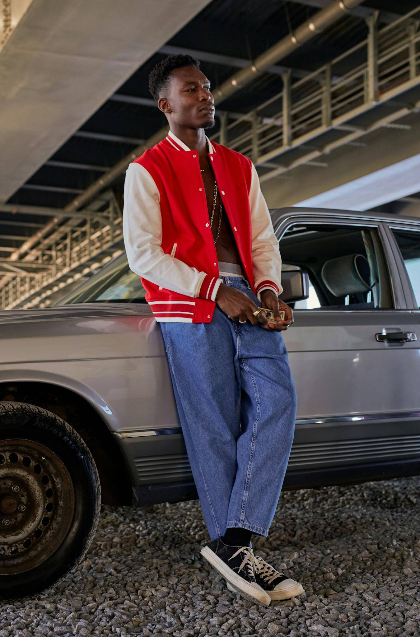 Young Man with a Handful of Cash Waiting Leaning Against an Old Mercedes Under a Bridge