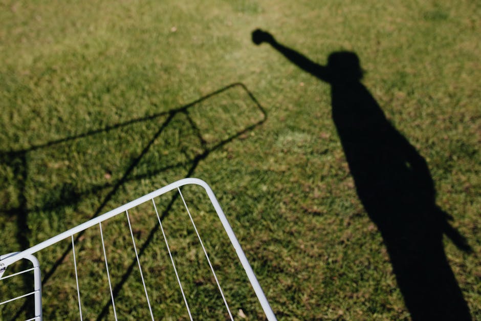 From above of metal dryer fragment with no clothes standing on grass outdoors and shadow of person imitating clothes hanging on drying rack on sunny summer day