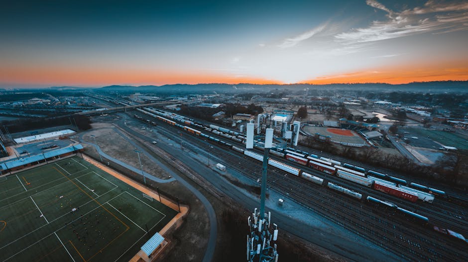 Aerial view of industrial district of Chattanooga city with green rugby fields and modern cell tower located near railroad tracks against sunset sky