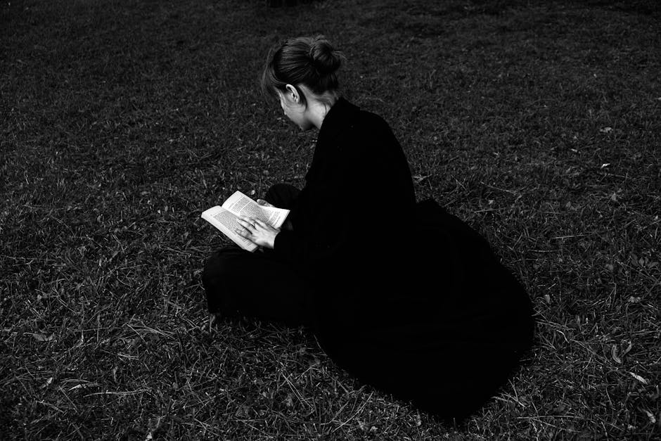 A woman sitting on the grass reading a book