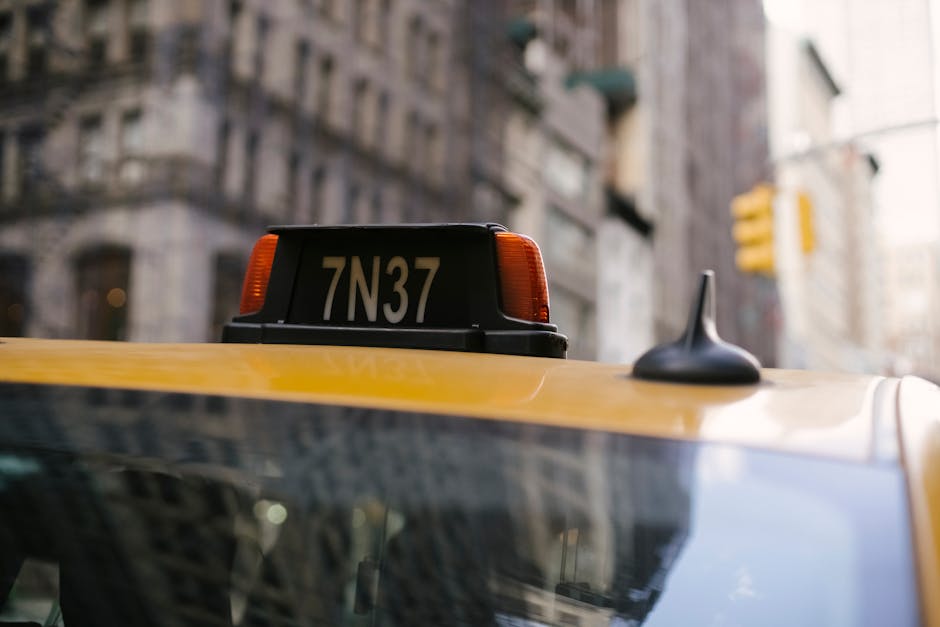 Sign on roof of yellow cab with numbers and letter located in city on street with residential buildings on blurred background