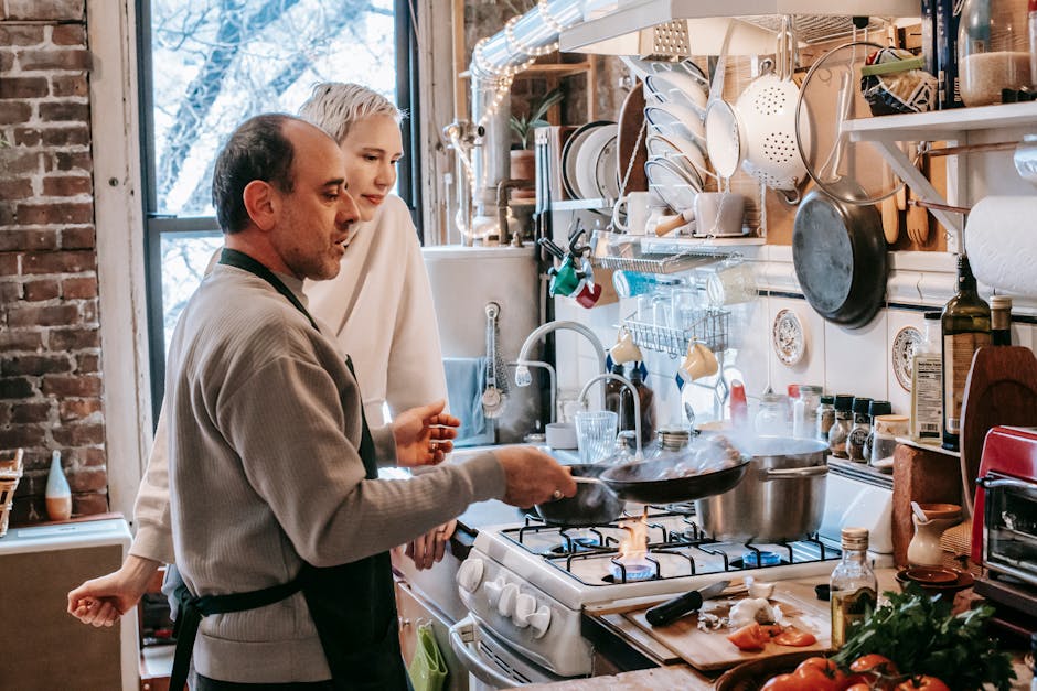 Concentrated husband in apron frying food on pan while cooking on gas stove with wife in kitchen