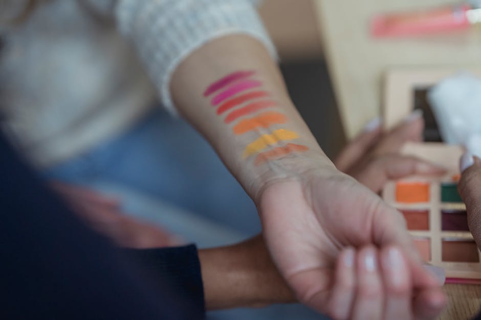 Faceless women applying multicolored eyeshadows on wrist for testing