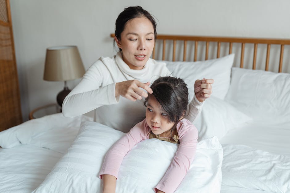 Asian mother adjusting hair of daughter on bed