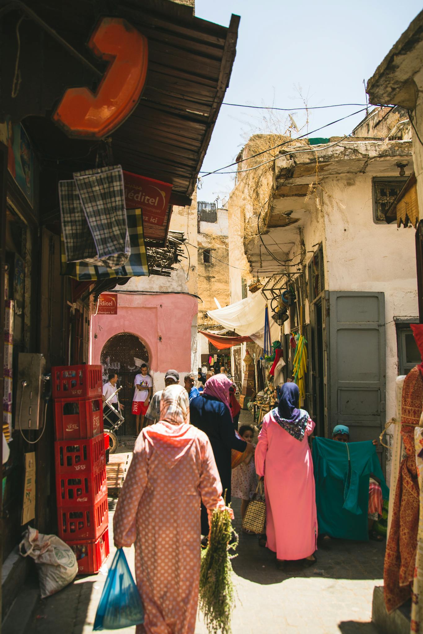 Back view unrecognizable Muslim females in traditional headscarves and modest clothes strolling in local outdoor bazaar on sunny day