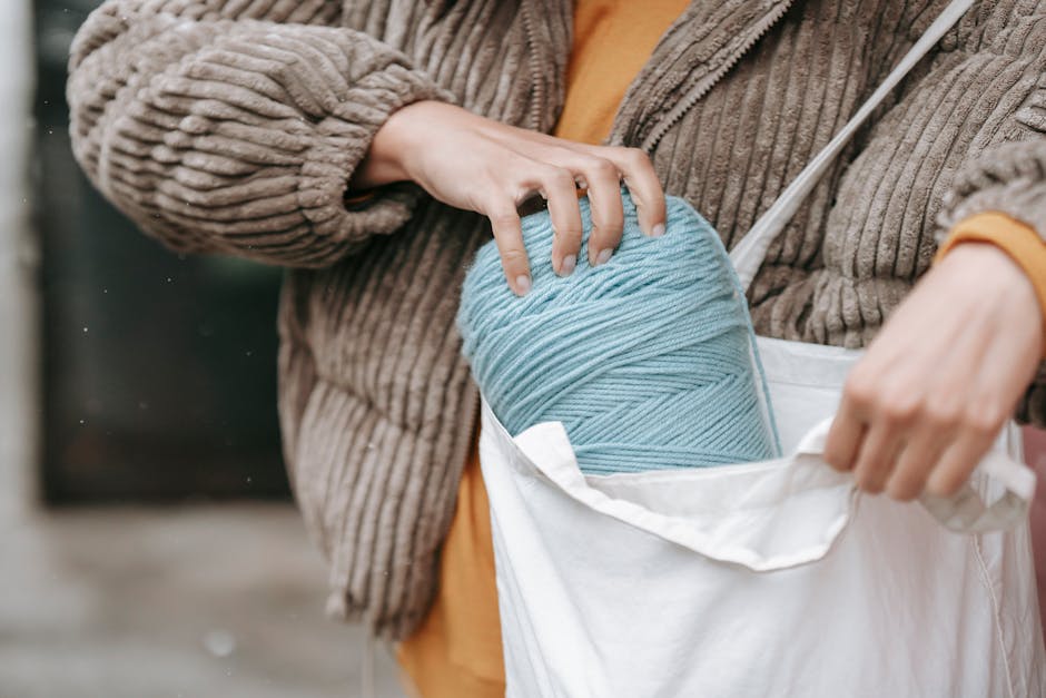 Crop female artisan in warm clothes putting skein in eco friendly bag on street in daylight