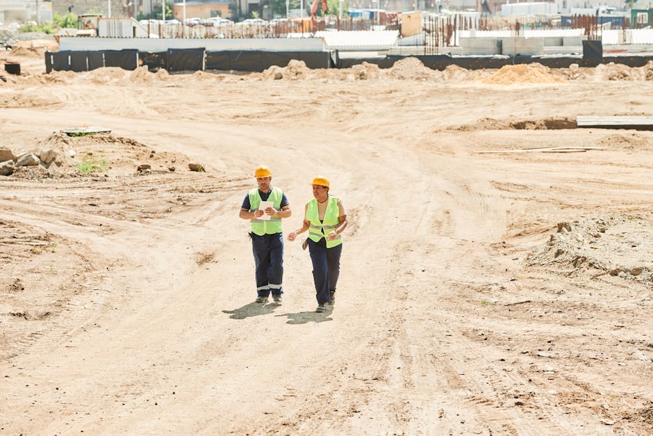 Man and Woman in Helmets and Reflective Vests Walking on a Construction Site
