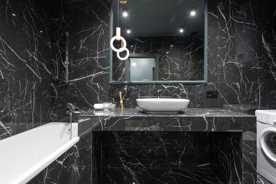 Acrylic bathtub and sink with washing machine in stylish bathroom with marble tiles on walls