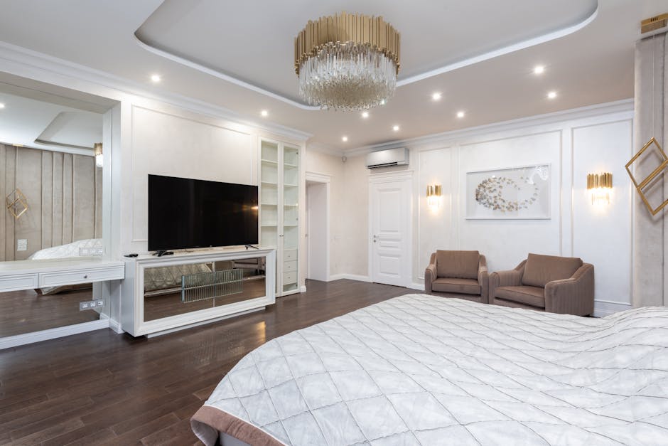 Interior of luxury bedroom with big bed and armchairs at wall and TV on cabinet under chandelier