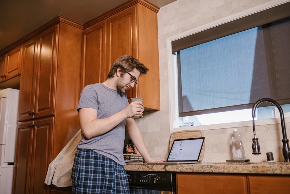 Man Holding a Mug Looking on His Laptop