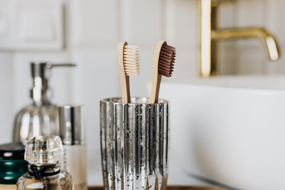 Eco friendly bamboo toothbrushes in silver glass placed in bathroom near sink and beauty products