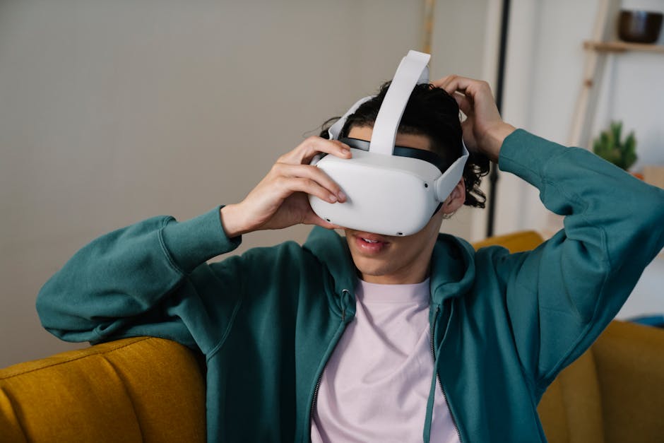 Male in hoodie putting on virtual reality headset while sitting on couch in light house