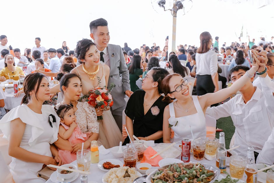 Group of happy friends in elegant clothes taking selfie with newlyweds on wedding party