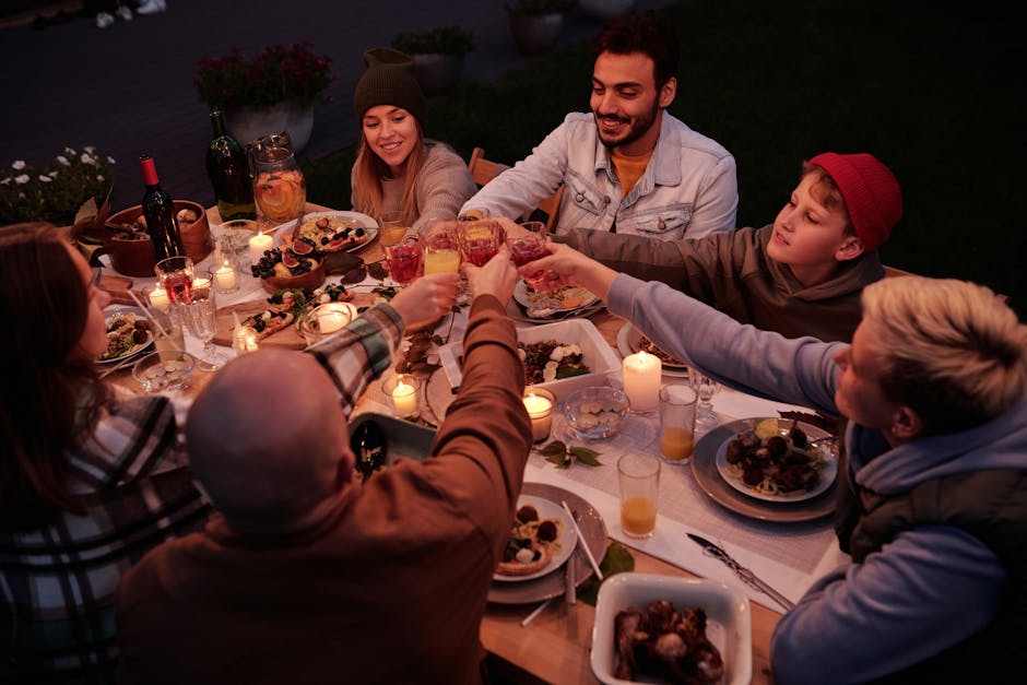 From above multiethnic people with children spending evening at dinner in dusky garden and cheering with drinks