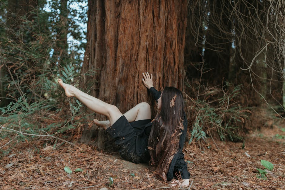 A Woman in Black Sitting on Ground Beside a Tree