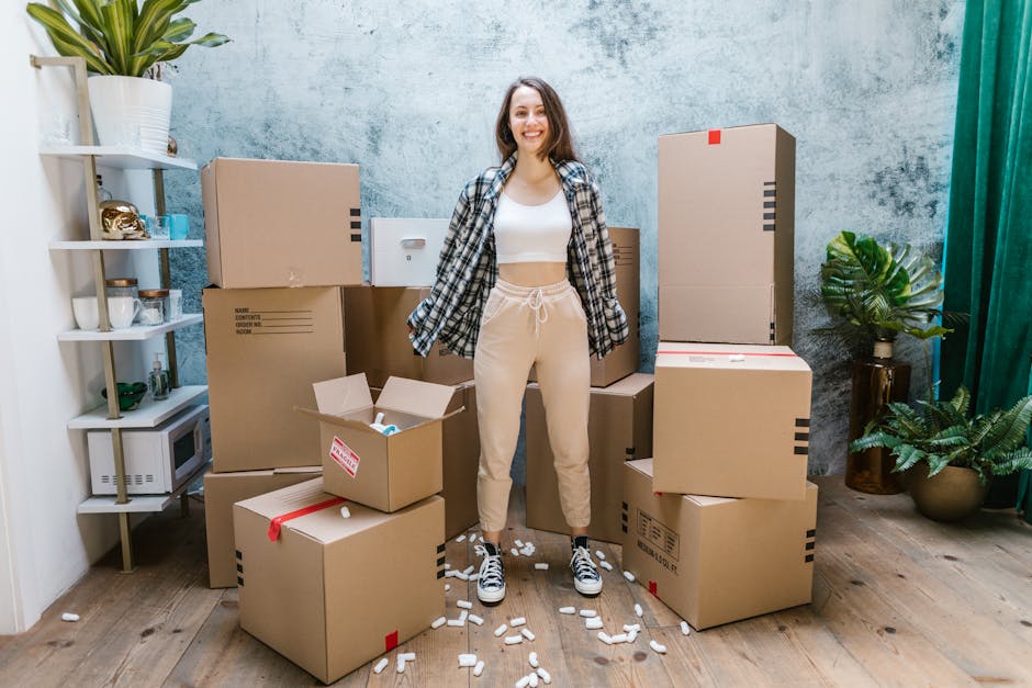 Photo of a Woman in a White Crop Top Standing Beside Cardboard Boxes