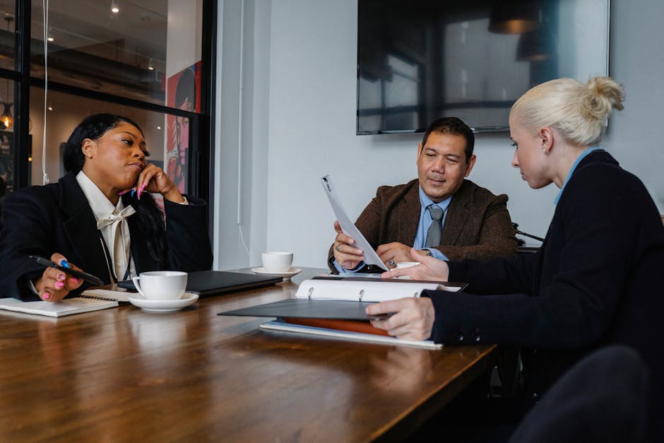 Multiethnic coworkers in formal wear sitting at table with documents and discussing details of business project